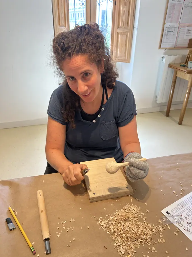 una participante tallando una cuchara de madera, con virutas sobre el banco